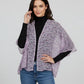 Woman wearing a light purple floral-patterned shawl over a black top and blue jeans on a plain background