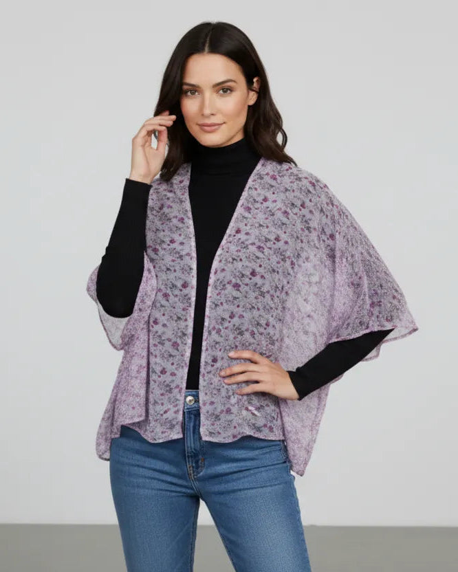 Woman wearing a purple floral kimono over a black top and blue jeans on a plain background