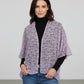 Woman wearing a purple floral kimono over a black top and blue jeans on a plain background