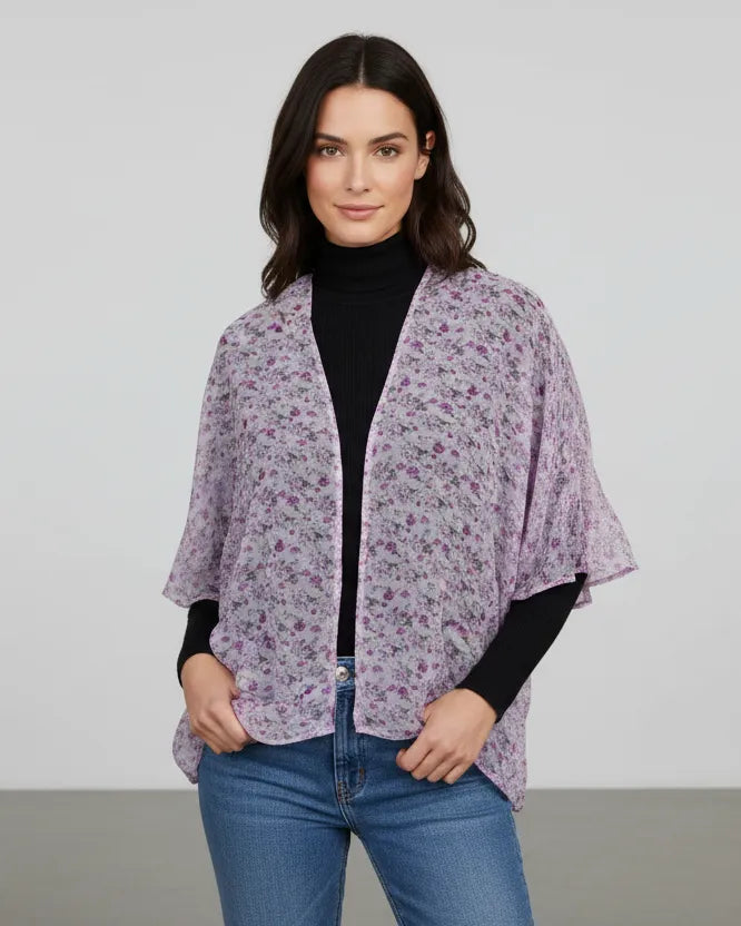 Woman wearing a purple floral kimono over a black top and blue jeans on a plain background