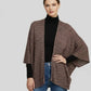 Woman wearing a brown patterned poncho over a black turtleneck and blue jeans on a light gray background