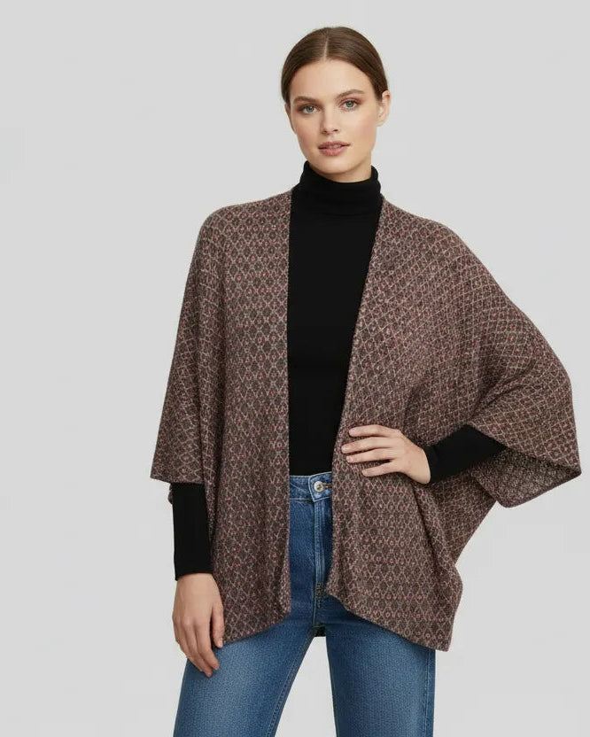 Woman wearing a brown patterned poncho over a black turtleneck and blue jeans on a light gray background