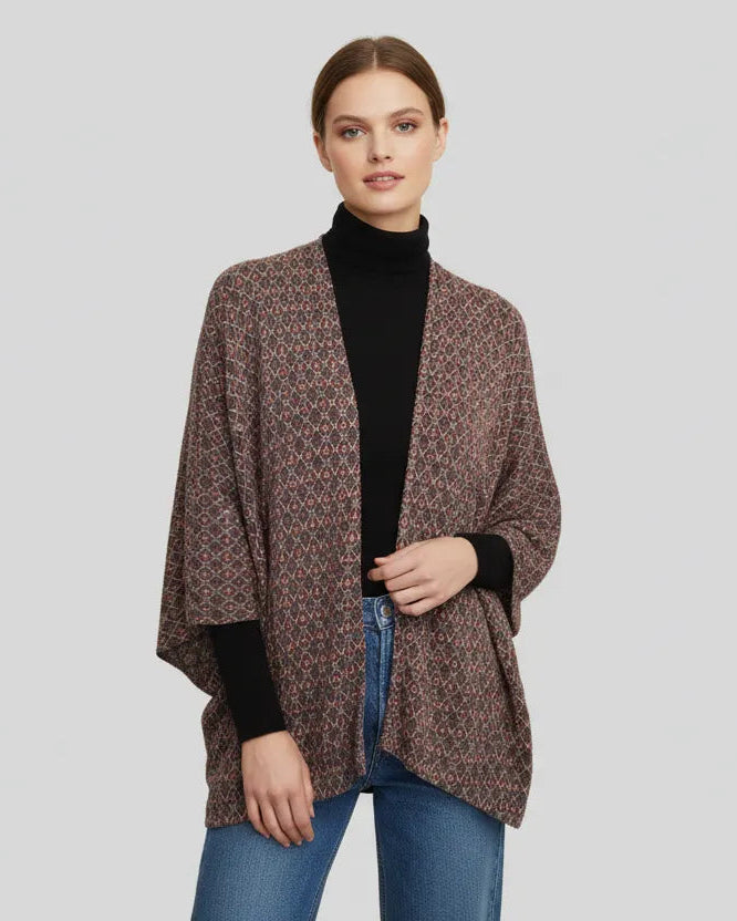 Woman wearing a brown patterned cardigan over a black turtleneck and blue jeans on a light gray background