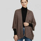 Woman wearing a brown patterned cardigan over a black turtleneck and blue jeans on a light gray background