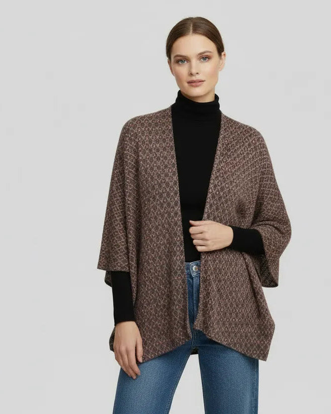 Woman wearing a brown patterned cardigan over a black turtleneck and blue jeans on a light gray background