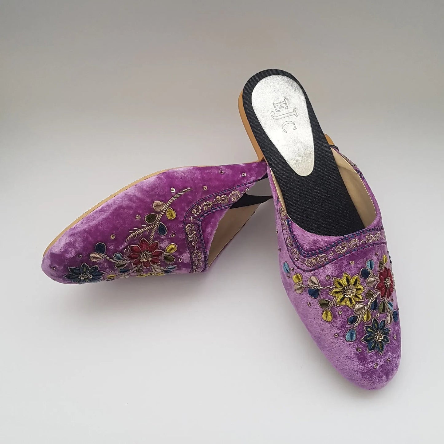 Purple embroidered mules on a light gray background