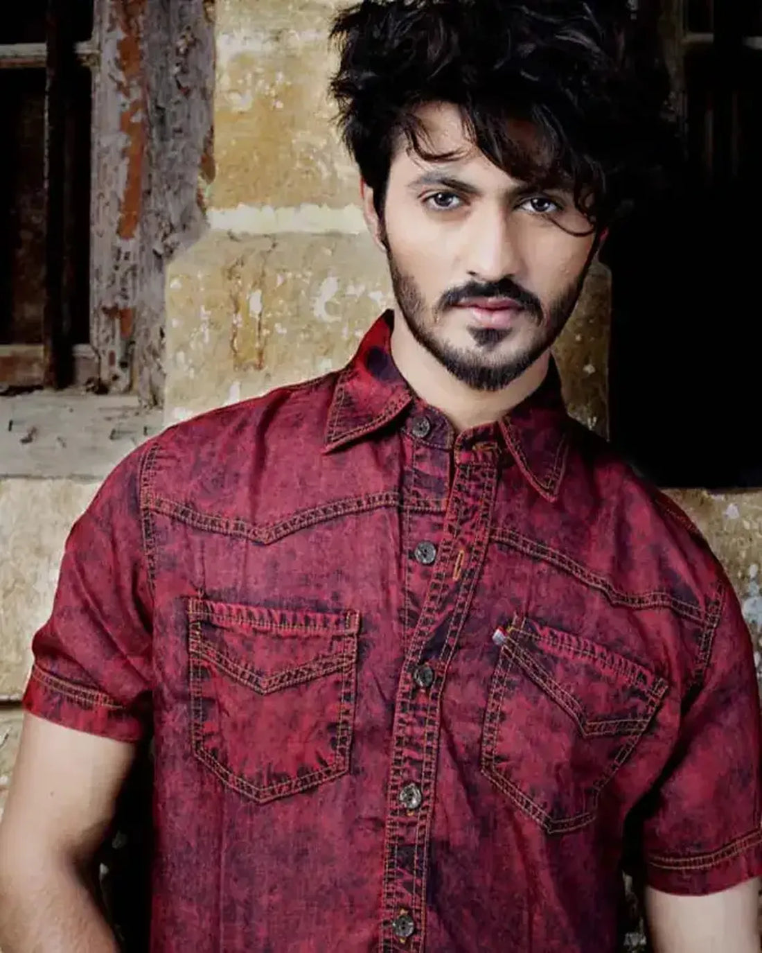 Man wearing a red denim shirt against a rustic background
