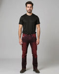 Man wearing a black t-shirt and maroon jeans against a gray background