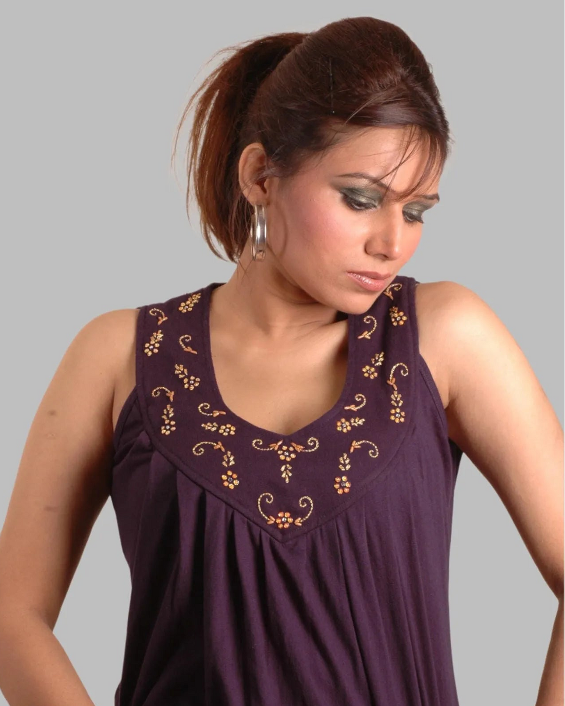 Woman wearing a purple sleeveless top with floral embroidery on a gray background