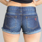 Person wearing blue denim shorts with a visible brand logo on a plain background