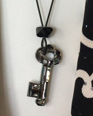 A silver-colored Swarovski crystal key pendant necklace displayed against a patterned background.
