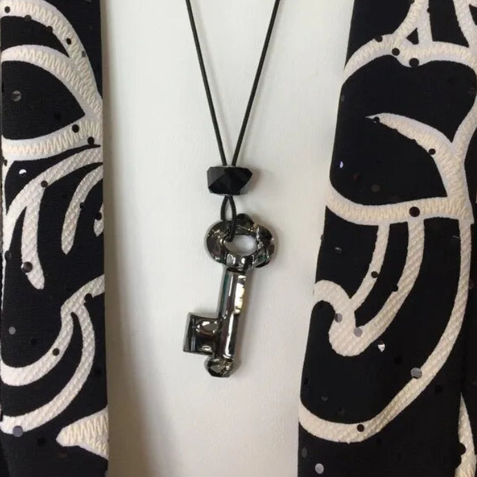 Necklace with a key pendant on a black and white patterned background