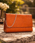 Tan clutch bag with a chain strap on a stone surface with a blurred natural background