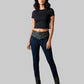 Woman wearing a black top and dark jeans with patterned cuffs on a gray background