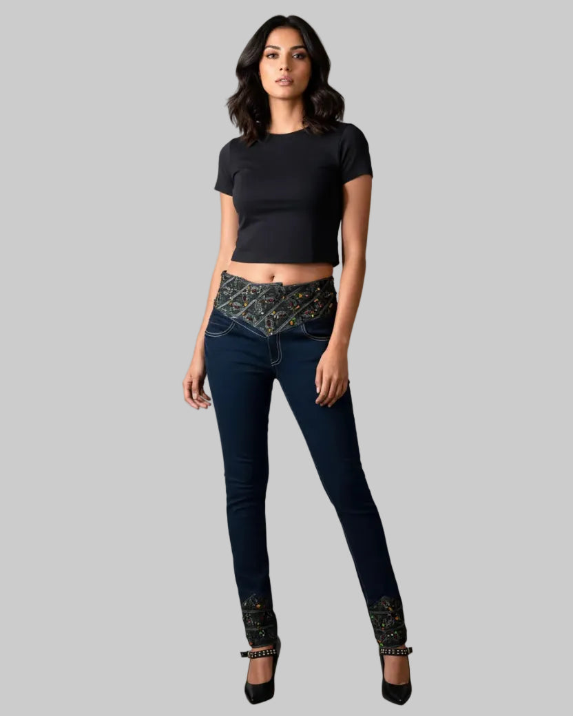 Woman wearing a black top and dark jeans with patterned cuffs on a gray background