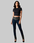 Woman wearing a black top and dark jeans with patterned cuffs on a gray background