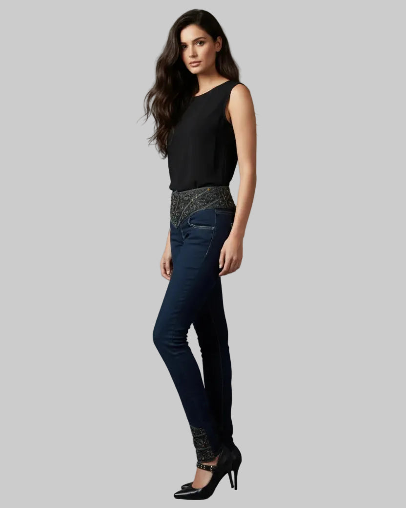 Woman wearing a black top and dark jeans with patterned cuffs on a gray background