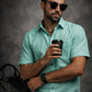 Man in teal shirt holding a coffee cup against a dark background