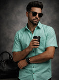 Man in teal shirt holding a coffee cup against a dark background