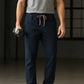 Person wearing navy jogger pants and a gray t-shirt holding dumbbells in a dark room.