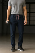 Person wearing navy jogger pants and a gray t-shirt holding dumbbells in a dark room.