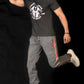 Person wearing a black t-shirt and gray pants with red accents, jumping against a black background