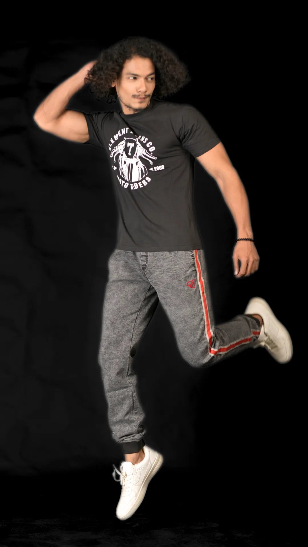 Person wearing a black t-shirt and gray pants with red accents, jumping against a black background