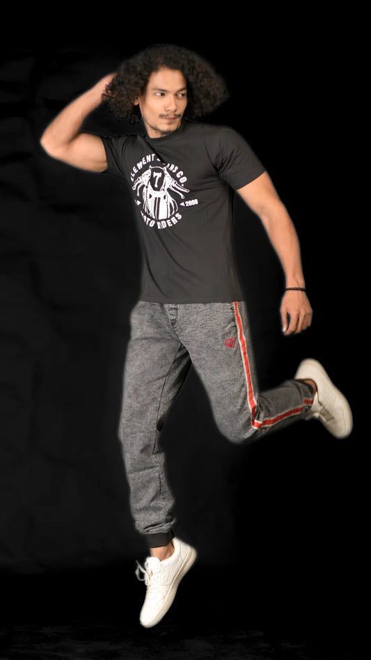 Person wearing a black t-shirt and gray pants with red accents, jumping against a black background