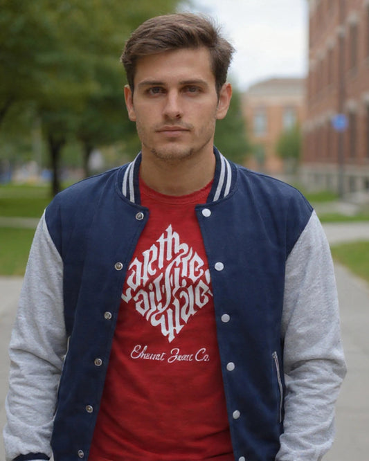 Man wearing a red shirt with white text and a blue and gray varsity jacket on a sidewalk.
