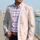 Man wearing a light-colored blazer over a plaid shirt by a waterfront.