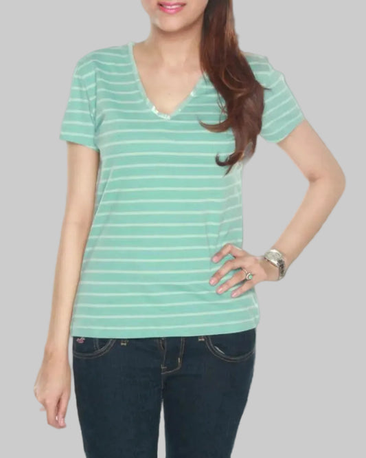 Woman wearing a green striped shirt and dark jeans on a gray background