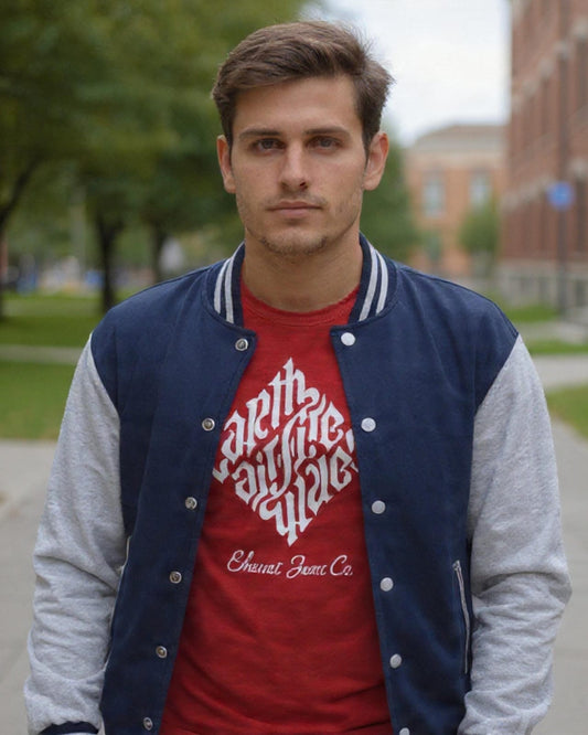Man wearing a red t-shirt with white text and a blue and gray varsity jacket on a sidewalk.