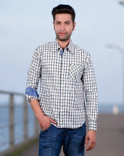 Man standing on a wooden pier wearing a checkered shirt and jeans.