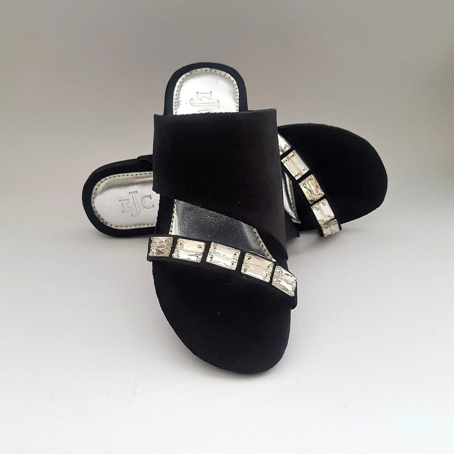 Black sandals with rhinestone embellishments on a light gray background
