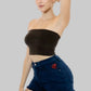 Woman wearing a black tube top and blue denim shorts with a visible brand logo on a beige background.