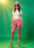 Woman wearing a white top, pink patterned pants, and a sun hat on a green background