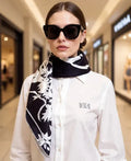 Woman wearing a black and white patterned scarf with a blurred mall background