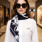 Woman wearing a white shirt and black and white patterned scarf with sunglasses in a blurred indoor setting
