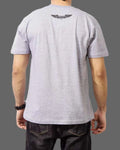 Person wearing a gray t-shirt with a logo on the back against a gray background
