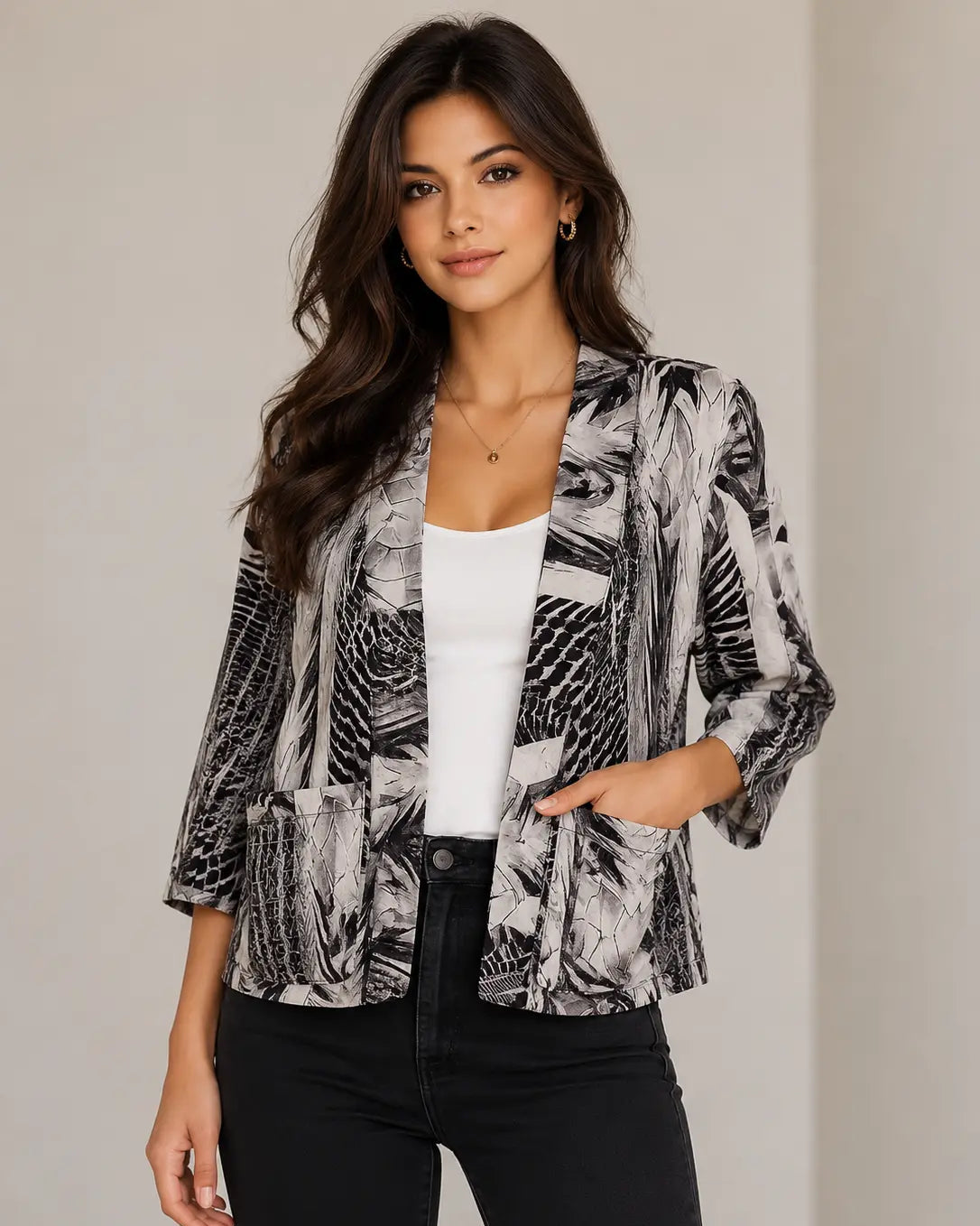 A woman modeling a black and white abstract print blazer style shrug over a white tank top and black pants, standing against a neutral beige background.