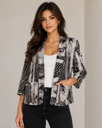 A woman modeling a black and white abstract print blazer style shrug over a white tank top and black pants, standing against a neutral beige background.