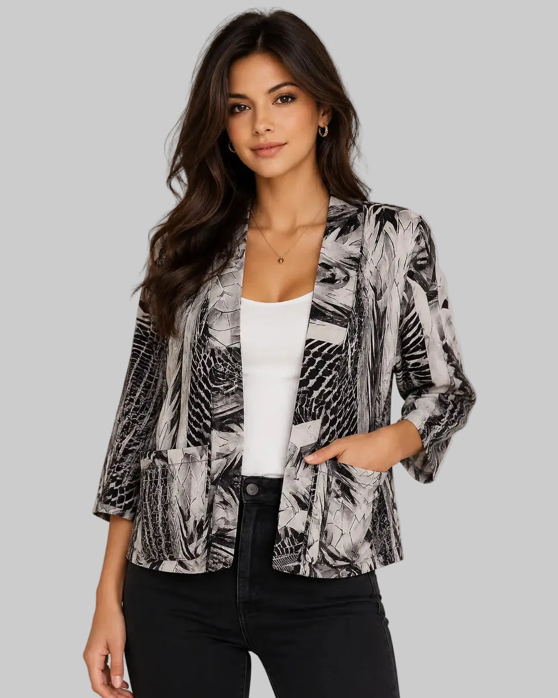 A woman modeling a black and white abstract print blazer over a white tank top and black pants, standing against a neutral beige background.