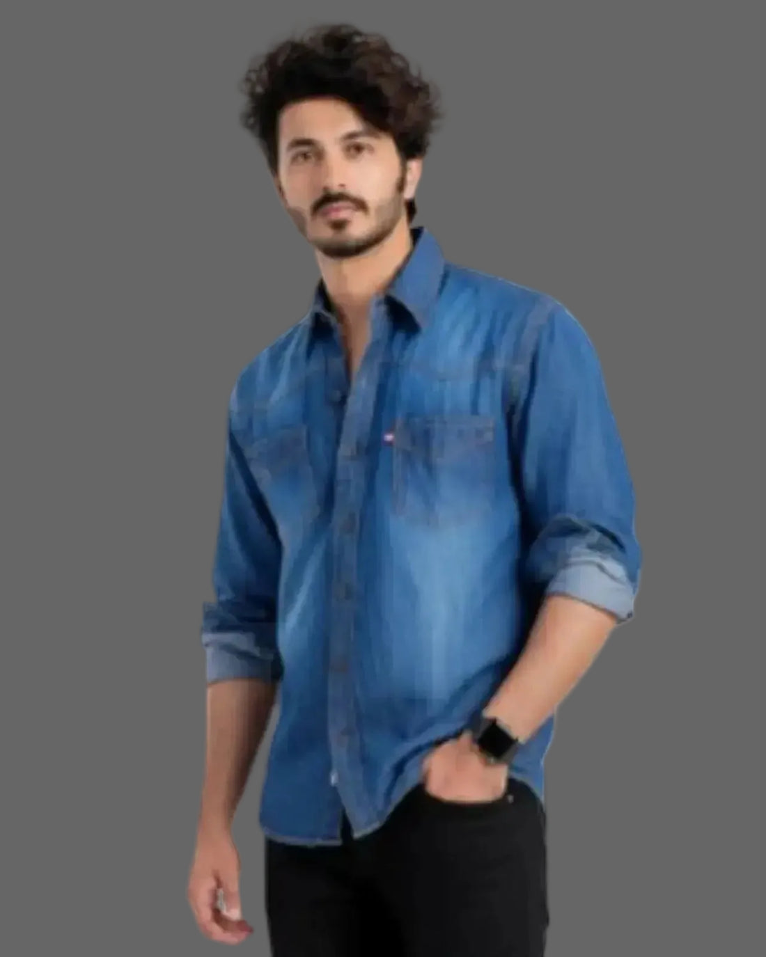 Man wearing a blue denim shirt and black pants sitting on a white background