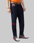 Person wearing dark blue jeans with a red patch on a plain background