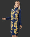 Woman wearing a denim dress with gold embroidery on a dark background