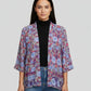 Woman wearing a patterned kimono-style jacket over a black top and jeans on a gray background