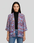 Woman wearing a patterned kimono-style jacket over a black top and jeans on a gray background