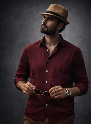 Man wearing a maroon shirt and brown hat against a dark background