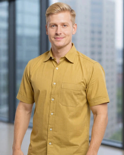 Man wearing a camel color handloom fabric camp shirt standing in front of a blurred indoor background