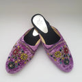 Pair of purple slippers with floral embroidery on a light gray background